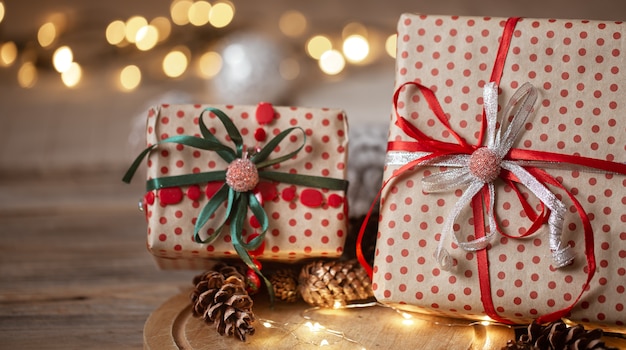 Christmas gifts packed in craft paper with ribbons, garland and decorative cones on blurred background.