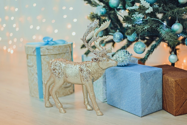 Photo christmas gifts and toy deer under the christmas tree in blue.