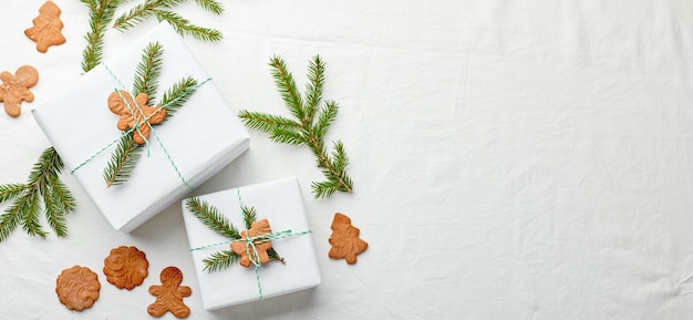 Christmas gifts wrapped in white paper and decorated with spruce sprigs and gingerbread cookies