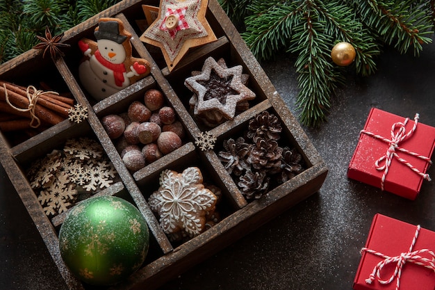 Рождественские пряники, печенье, орехи и праздничные украшения в деревянной коробке с елкой и подарками.