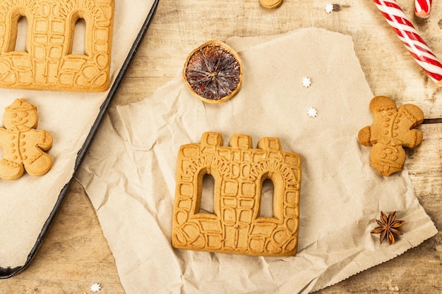 Christmas Gingerbread House and Gingerbread Men. Traditional festive New Year design, cooking process. Old wooden background, rustic style, top view