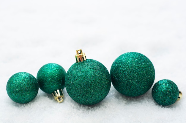 Christmas glittered green baubles isolated on snow. Winter greeting card.