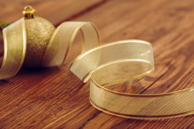 Christmas golden ball amid the yellow ribbon spiral on Wooden background