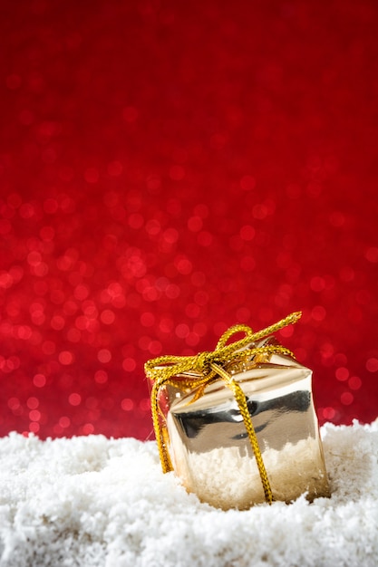 Christmas golden gift box ornaments on snow and red glitter surface 