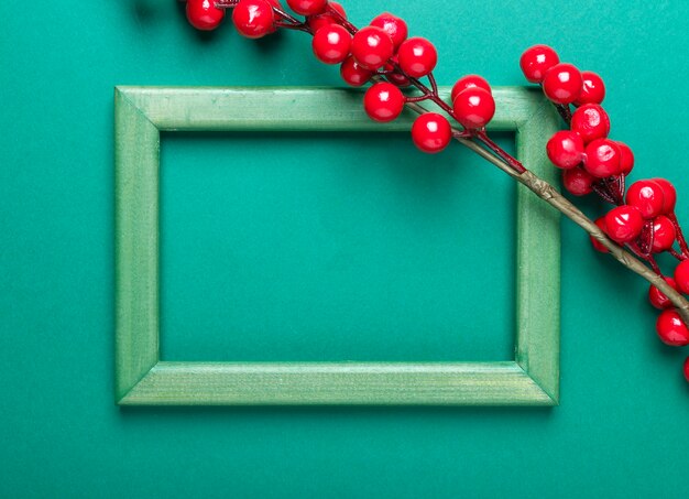 Christmas green background with frame with place for text or copy space with twig of red berries or viburnum.