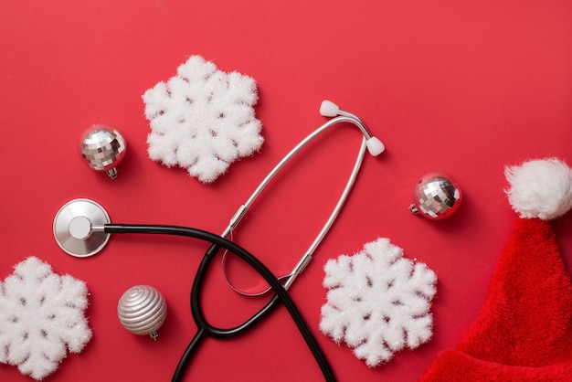 Фото Рождественская открытка для медиков. традиционные рождественские и новогодние украшения и медицинский стетоскоп на красном фоне
