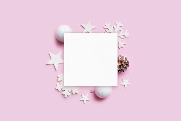 Christmas greeting card mockup with Christmas decorations on pastel pink desk. Blank paper for greeting text. Top view, flat lay