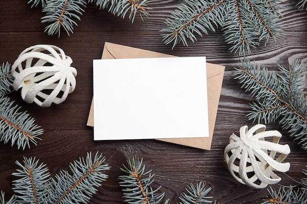 クリスマス グリーティング カード モックアップ封筒緑のモミの木の枝と茶色の木製の背景平面図上の装飾冬の装飾が施された白い新年のホリデー カードが横たわっていた