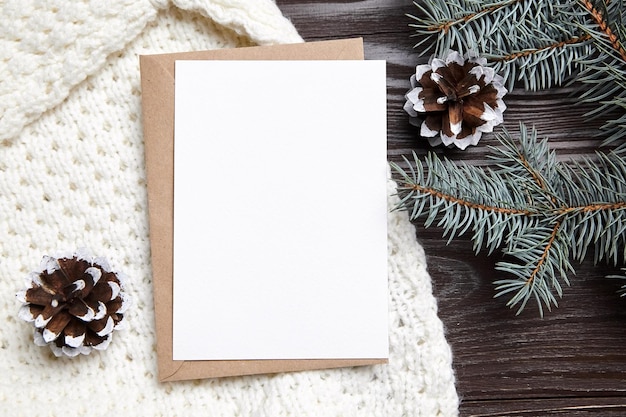 Photo christmas greeting card mockup with envelope knitted sweater green fir tree branches and cone on brown wooden background top view flat lay blank new year holiday card