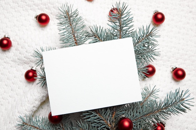 Christmas greeting card mockup with fir tree branches and red balls on white knitted pullover background top view