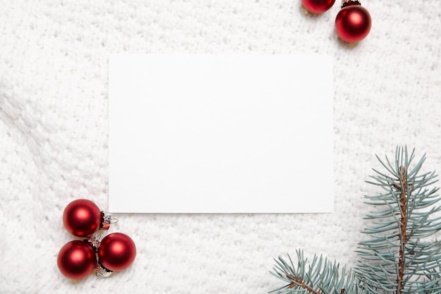 Christmas greeting card mockup with fir tree branches and red balls on white knitted pullover background top view