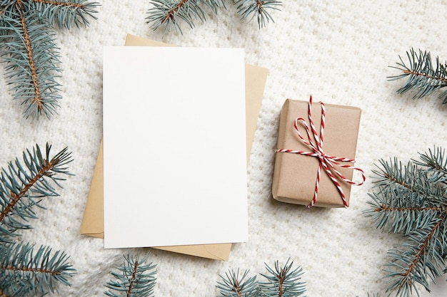 Макет рождественской открытки с подарочной коробкой и еловыми ветками на фоне белого вязаного пуловера, вид сверху, плоская планировка