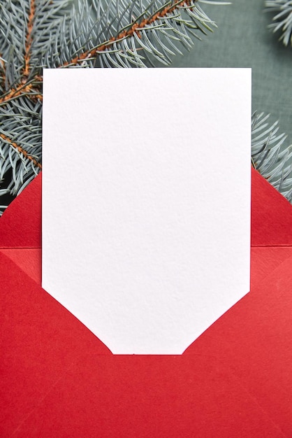 Christmas greeting card mockup with red envelope and fir tree branches on green background top view flat lay