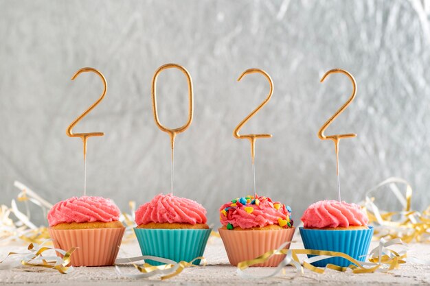 Christmas greeting card with cupcakes and gold sparklers numbers 2022. Holiday muffins with pink buttercream frosting.