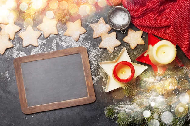 Christmas greeting card with fir tree gingerbread cookies and candles on stone background Top view flat lay with chalkboard for your xmas greetings