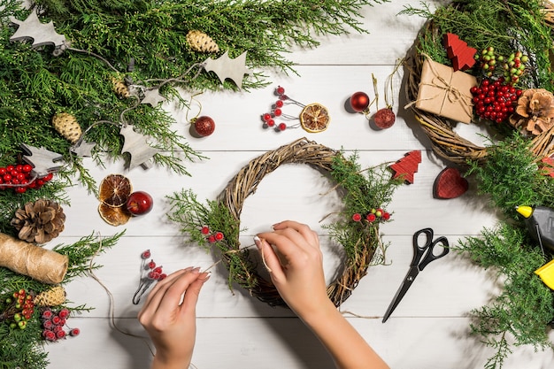 クリスマス手作りのDIYの背景。クラフトクリスマスリースやオーナメントを作る。休日の装飾のための女性のレジャー、ツール、装身具。女性の手で白い木製のテーブルの平面図です。