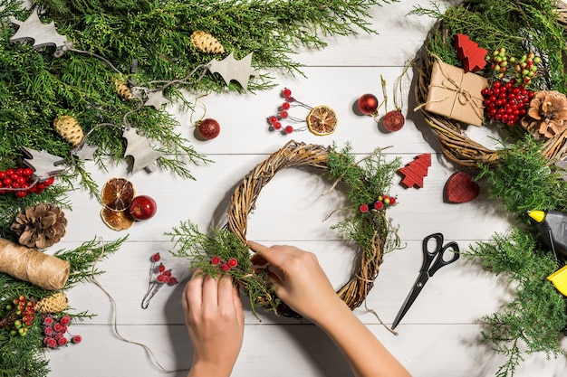 クリスマス手作りのDIYの背景。クラフトクリスマスリースやオーナメントを作る。休日の装飾のための女性のレジャー、ツール、装身具。女性の手で白い木製のテーブルの平面図です。