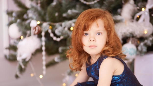 Ragazza felice di natale bambino attraente di lusso con capelli rossi miracolo di natale l'albero verde accende il bokeh