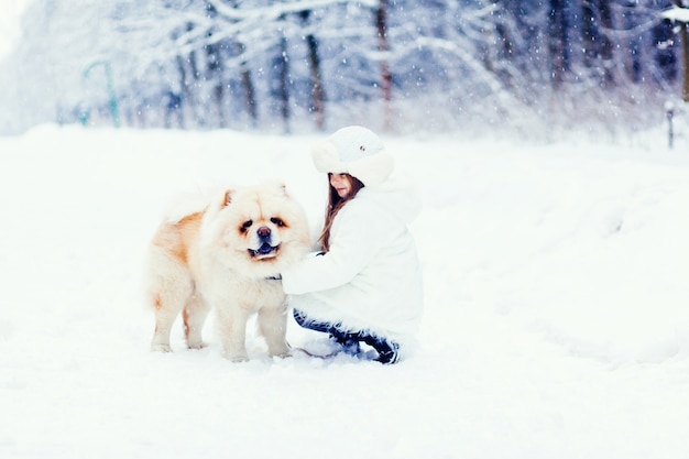 Рождественская счастливая девушка играет с собакой чау-чау на снегу в зимний день