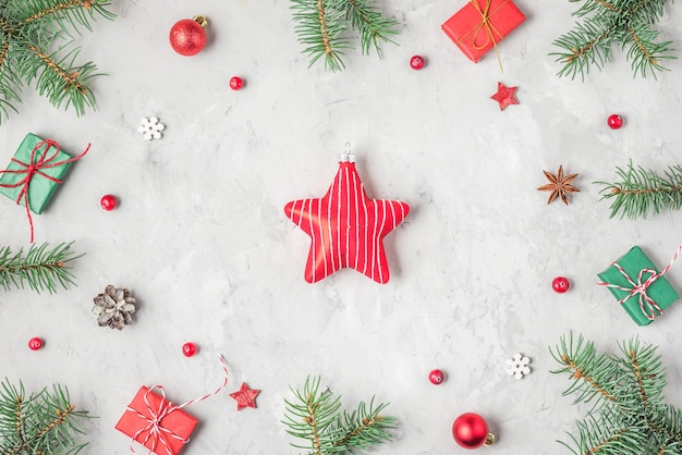 Christmas or Happy New Year composition. Star toy in frame made of fir tree, red decorations and gift boxes on concrete background. top view. flat lay with copy space