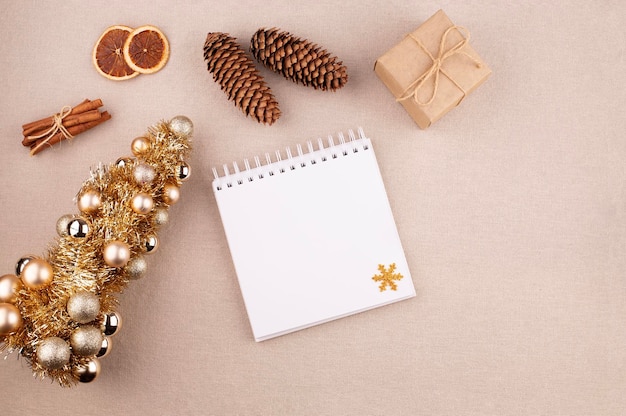 Рождественский праздничный фон с дневником и золотистым деревом коричневые палочки и подарок, завернутые в крафт-бумагу сушеные апельсины на льняной ткани фон плоское пространство для копирования