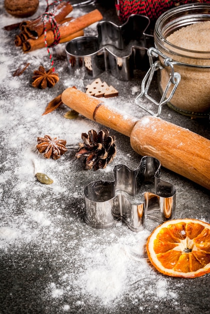 クリスマス、休日の料理。材料、スパイス、乾燥オレンジ、焼き型、クリスマスデコレーション（ボール、モミの木の枝、コーン）、黒い石のテーブル、