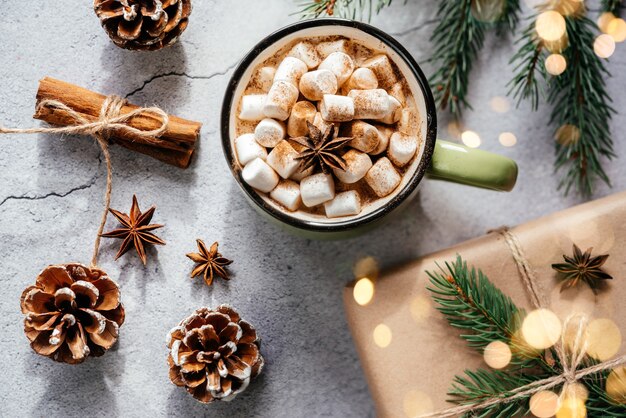 Layout creativo per le vacanze di natale con tazza viola di marshmallow cioccolata calda pino e pigne