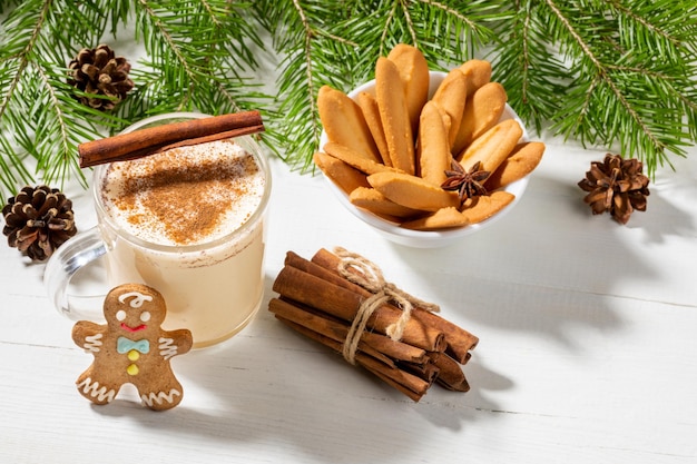 Christmas holiday drink homemade eggnog with cinnamon and ginger cookies on white wooden backdrop.