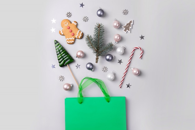 Concetto di shopping vacanze di natale. borsa verde con regali festivi, bastoncino di zucchero, dolcetti, decorazioni, coriandoli glitter