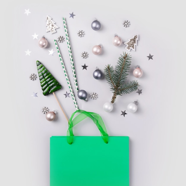 Christmas holiday shopping . Green bag with festive purchases, decor, glitter confetti on grey .