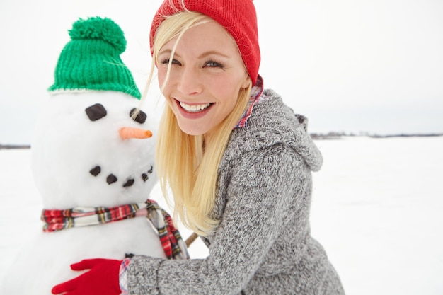 Photo christmas holiday and woman with snowman in winter vacation portrait happy building with snow and celebration festive spirit with xmas tradition outdoor happiness and celebrate with nature