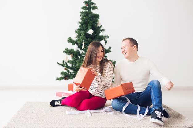 クリスマス、休日、お祝いのコンセプト-ハンサムな若い男とかなり若い女性がカーペットの上に座って、ギフトボックスを保持しています。