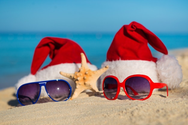 Фото Рождественские каникулы и романтический новый год на море. санта-шляпы и солнцезащитные очки на песчаном пляже