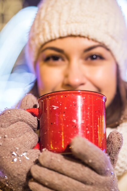 크리스마스 휴일 겨울에 야외에서 뜨거운 커피 한잔과 함께 따뜻한 옷을 입은 아름다운 웃는 여자