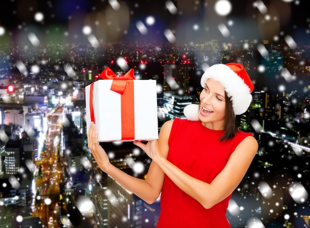 Фото Рождество, праздники, праздник и концепция людей - улыбающаяся женщина в красном платье с подарочной коробкой на заднем плане