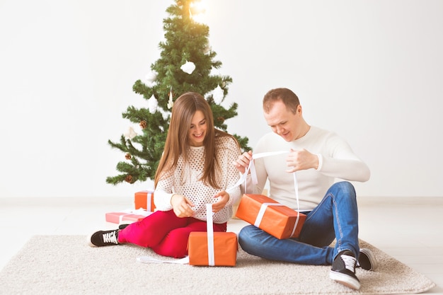 Christmas, holidays and celebration concept - Handsome young man and pretty young woman sitting on the carpet and are holding a gift boxes.