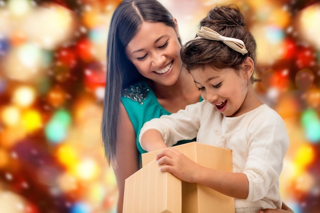 Christmas, holidays, celebration, family and people concept - happy mother and child girl with gift box over red lights background