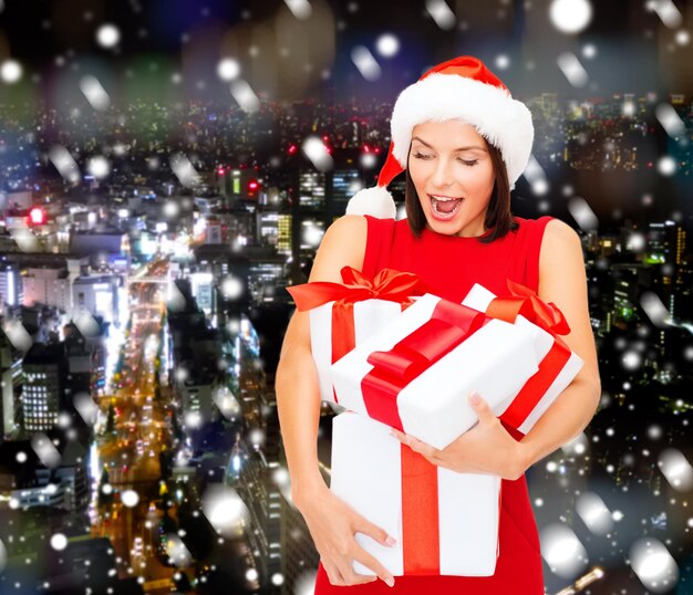 クリスマス、休日、お祝い、人々の概念-背景の上のギフトボックスと赤いドレスの笑顔の女性