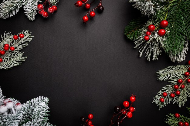 Foto composizione di vacanze di natale con bacche rosse e rami di abete su sfondo nero con spazio di copia per il tuo testo