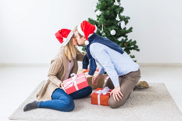 Concetto di natale e festività - giovani coppie felici che indossano cappelli di babbo natale che aprono i regali a casa.