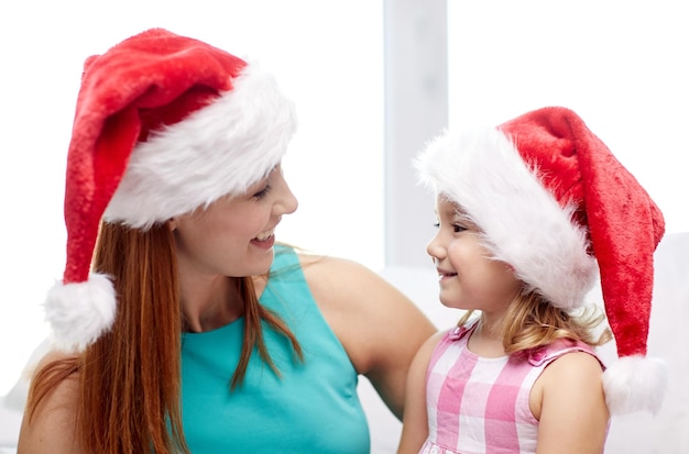 크리스마스, 휴일, 가족, 어린 시절, 그리고 사람들의 개념 - 집에서 산타 모자를 쓴 행복한 엄마와 어린 소녀