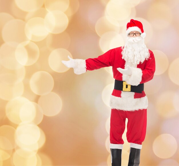 クリスマス、休日、ジェスチャー、人のコンセプト-ベージュのライトの背景にサンタクロースの衣装を着た男