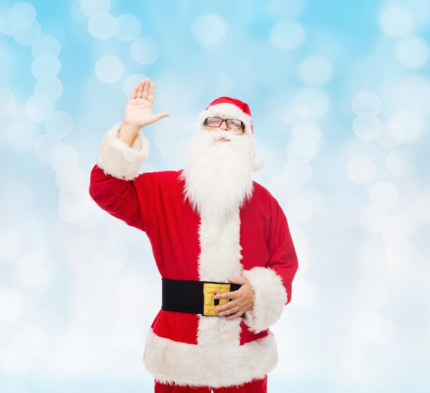 크리스마스, 휴일, 몸짓, 그리고 사람들의 개념 - 산타클로스 의상을 입은 남자가 파란 불빛 배경 위에 손을 흔들고 있다