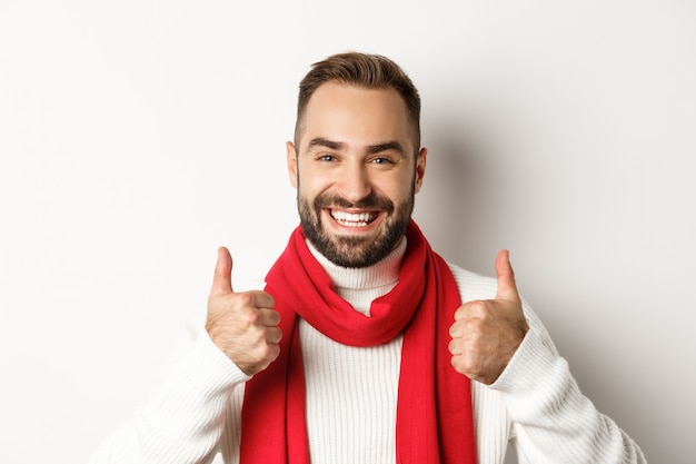 Vacanze di natale. bel ragazzo soddisfatto che mostra i pollici in su, mi piace e approva, godendosi fantastiche vacanze invernali, sfondo bianco.