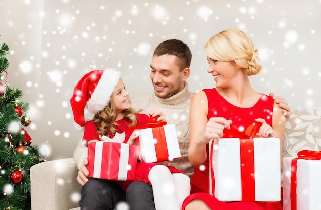 クリスマス、休日、幸福と人々の概念-自宅にたくさんのギフトボックスがあるサンタヘルパー帽子の笑顔の家族