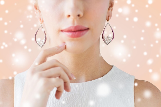 christmas, holidays, jewelry, people and luxury concept - close up of beautiful woman face with pearl earrings over beige background