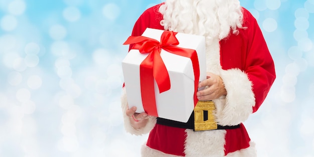 christmas, holidays and people concept - close up of santa claus with gift box over blue lights background