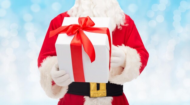 christmas, holidays and people concept - close up of santa claus with gift box over blue lights background