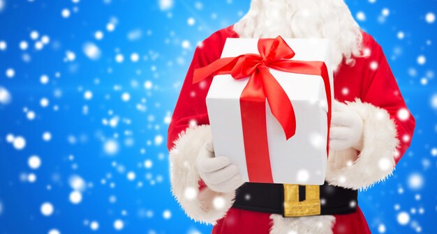 christmas, holidays and people concept - close up of santa claus with gift box over blue snowy background