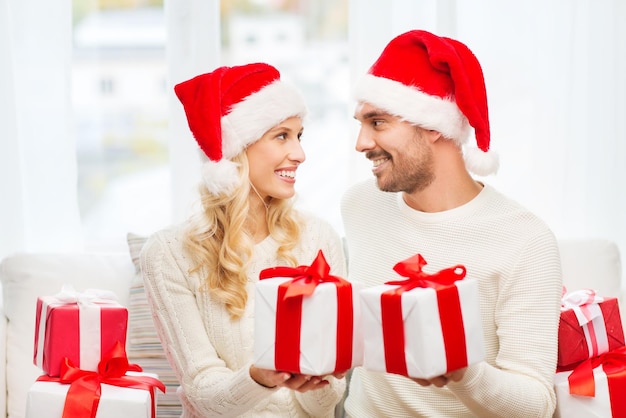 christmas, holidays and people concept - happy couple in santa hats exchanging gifts at home